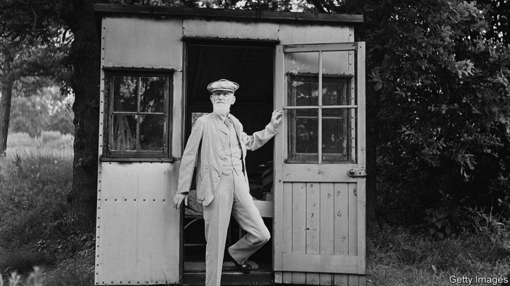 Black-and-white photo of a man with beard emerging from shed