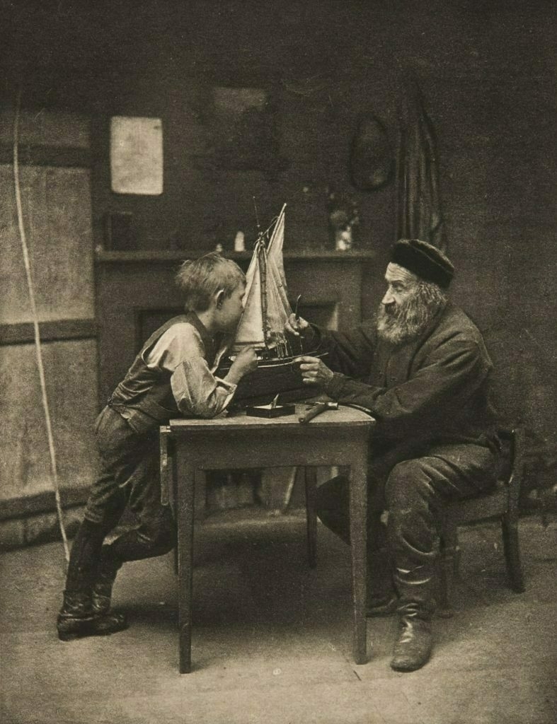 Vintage photograph of an old man building a model ship with a young boy